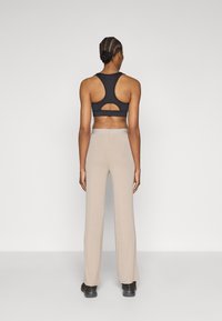 Musta urheiluliivit, joissa on racerback-malli ja avonainen leikattu yksityiskohta, yhdistettynä beigenvärisiin leveälahkeisiin housuihin ja mustiin jalkineisiin.