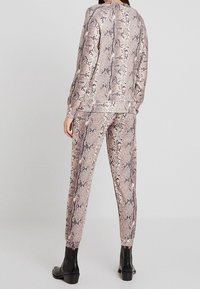 Dwuczęściowy strój z jasnobrązowym wzorem w węża. Góra ma długie rękawy, a spodnie są zwężane i mają elastyczny pas.