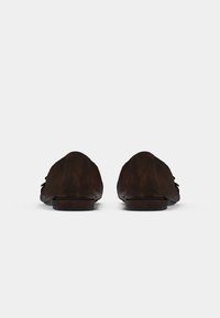 Mocassins en cuir marron foncé avec un bout arrondi, une texture douce et un détail de nœud subtil sur le devant. Design minimaliste, semelle plate.
