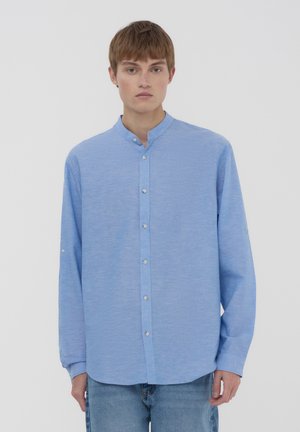 Camicia button-down a maniche lunghe di un azzurro chiaro con colletto alla mandarino. Tessuto liscio, due bottoni ai polsini e taglio dritto.