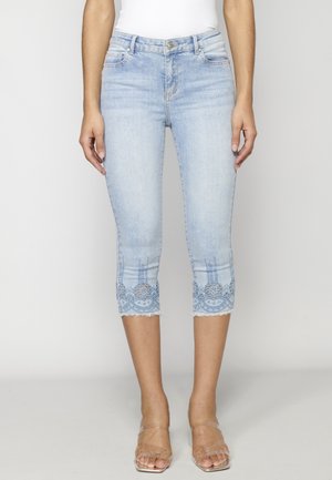 Jasnoniebieskie krótkie rurki z wyszywanymi kwiatowymi koronkowymi brzegami, noszone z sandałami na wysokim obcasie z przezroczystymi paskami i białym topem.