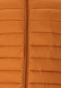 Orange pufferväst med vertikal quiltning, förankrad med en central dragkedja och en logotyp i övre högra hörnet. Slät, vadderad textur.