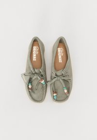 Chaussons en suède vert de style mocassin avec une semelle plate, ornés de perles décoratives et d'un nœud à l'avant, dotés d'une semelle intérieure de marque.