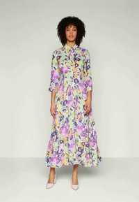 Vestido maxi floral com uma base verde-claro, padrões roxos, rosas e amarelos, mangas longas e fecho frontal com botões.