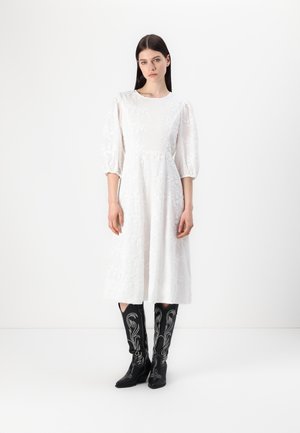 White floral embroidered dress with puffed sleeves, mid-length hem, paired with tall black cowboy boots featuring white stitching details.