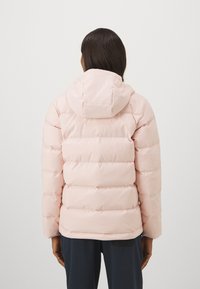 Svijetloružasta puffer jakna s kapuljačom, koja ima kviltani dizajn i blago labav kroj. Materijal djeluje glatko i izolirano.