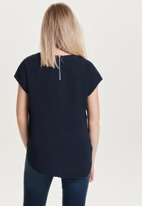 Námořnický top s krátkým rukávem a jemnou texturou, zaobleným lemem a stříbrným zipem na zádech. Nosit s tmavými džíny.