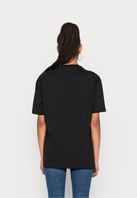 T-shirt en coton noir à manches courtes, coupe décontractée et col rond. Pas de logos ni de motifs visibles, porté avec un jean en denim bleu.