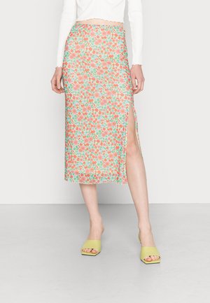 Saia midi floral com fundo verde, flores vermelhas e rosas, fenda lateral, combinada com sandálias de salto bloco verdes.