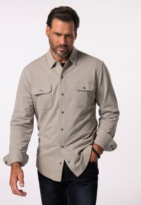 Camicia button-up grigia chiara con colletto, due tasche sul petto e maniche arrotolate, realizzata in un tessuto testurizzato. Jeans scuri completano l'outfit.