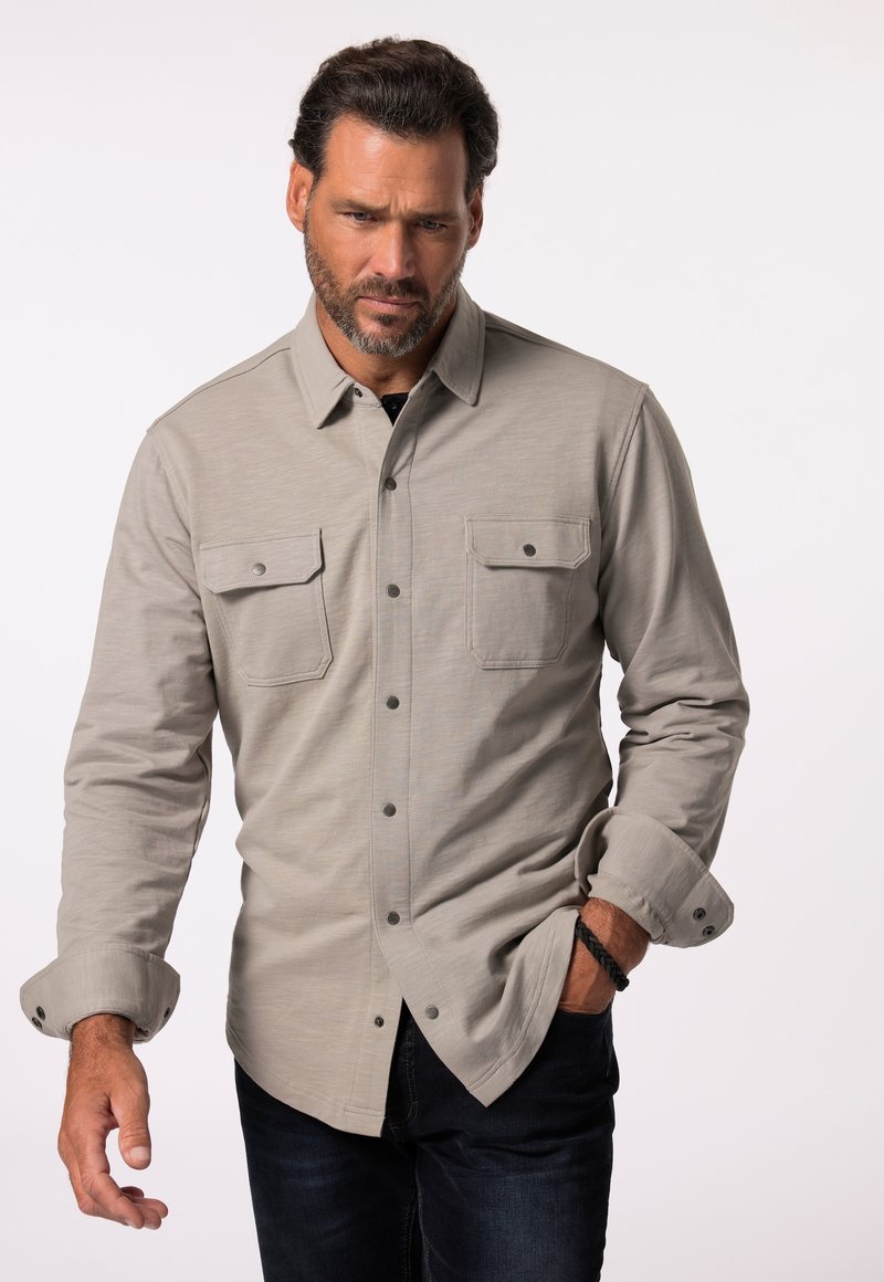 Lichtgrijze button-up shirt met een kraag, twee borstzakken en opgestroopte mouwen, gemaakt van een gestructureerde stof. Donkere spijkerbroeken maken de outfit compleet.