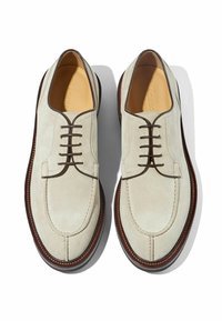 Scarpe in suede bianco con lacci marroni e suole in pelle marrone a contrasto. Presentano una punta rotonda e dettagli di cucitura minimali.