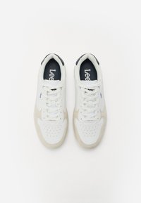 Zapatillas blancas y beige claro con una parte superior de cuero suave, puntera perforada y acentos en azul marino contrastantes. Diseño de cordones en el frente.