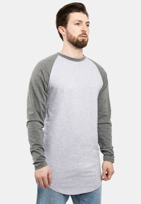 Grau-weißes Langarmshirt mit Raglanärmeln, abgerundetem Saum, weichem Material und lässiger Passform.