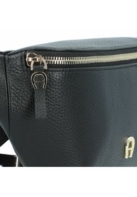 Borsa in pelle nera con texture, dotata di una cerniera dorata e di un emblema dorato coordinato sulla parte anteriore.