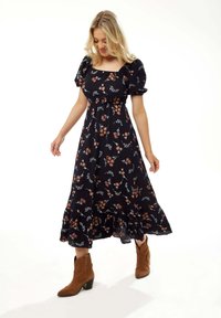 Black floral maxi dress with puff sleeves, featuring colorful flower patterns and a flared hem. Paired with brown cowboy boots.