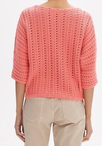 Koraalrode gebreide trui met een gestructureerd gestreept patroon, driekwart mouwen en een losse pasvorm, met opengewerkte details en een ronde halslijn.