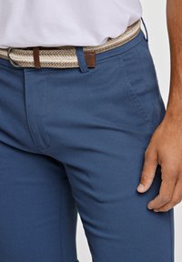 Pantaloni blu con trama, dal design aderente, caratterizzati da una cintura intrecciata beige accentuata da hardware in pelle marrone.