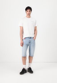 White cotton t-shirt with small logo, light blue denim shorts, black sneakers with white soles, and white crew socks.