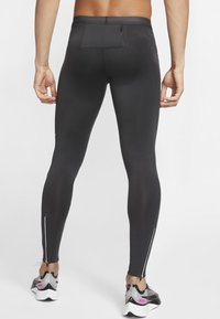 Mężczyzna ubrany w czarne legginsy sportowe z tylną kieszonką na zamek błyskawiczny oraz zamkami przy kostkach, stojący, pokazany z tyłu.