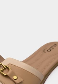 Sandale beige enfilable avec détail de boucle dorée et semelle intérieure rembourrée sur fond blanc.