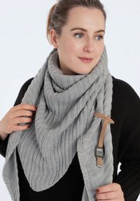 Grijze gebreide sjaal met een gestructureerd ribbelpatroon, gedrapeerd in een driehoekige vorm. Voorzien van een leren label met "Knit Factory" branding.