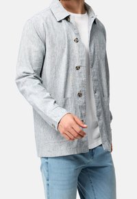 Light gray button-up jacket with a textured pattern, shirt collar, and two front pockets. Paired with a white t-shirt and light blue jeans.