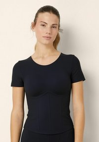 Top nero a maniche corte, aderente, con scollatura rotonda, dotato di un busto strutturato e dettagli di cuciture verticali, realizzato in un tessuto liscio ed elastico.