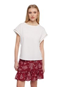 Top bianco a maniche corte con scollatura rotonda e bordo decorativo sulle maniche, abbinato a una gonna a balze in bordeaux con stampa floreale.