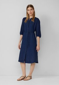Abito blu navy a lunghezza ginocchio con abbottonatura frontale, maniche arricciate, vita con fiocco e spacchi laterali; realizzato in un tessuto leggero.