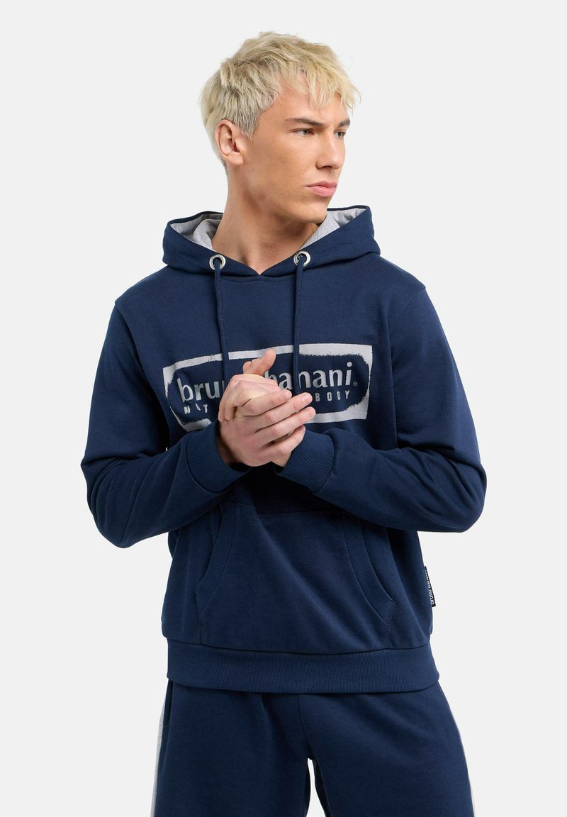 Marineblaue Kapuzenjacke mit weißem Logo, verstellbare Kapuze, Fronttasche und gerippten Bündchen. Weicher Stoff mit lässigem Schnitt, kombiniert mit passenden Hosen.