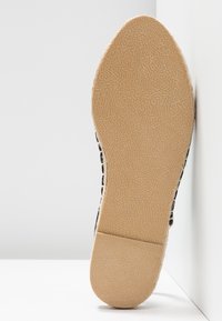 Semelle de chaussure à motifs noir et blanc avec une base en caoutchouc texturé beige. Design simple avec un bout arrondi et un profil plat.