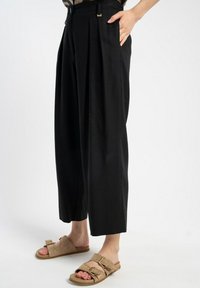 Czarne, plisowane spodnie z wysokim stanem i bocznymi kieszeniami. Gładki materiał o lekko połyskującej powierzchni. W komplecie z beżowymi klapkami z metalowymi ćwiekami.