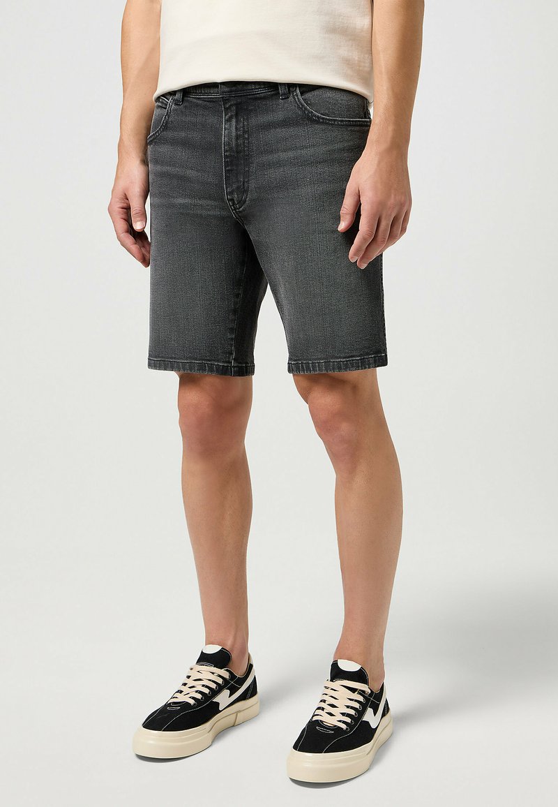 Shorts de mezclilla gris con corte recto, cinco bolsillos y trabillas para el cinturón. Combinados con zapatillas negras y cremosas con cordones y acentos de logo.