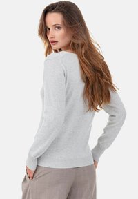 Hellgrauer Strickpullover mit weicher Struktur, Rundhalsausschnitt und gerippten Bündchen. Von hinten getragen über beigefarbenen Hosen.