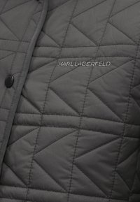 Jachetă gri matlasată, realizată dintr-un material ușor, având un model diagonal, închidere cu capse și logo brodat "KARL LAGERFELD".