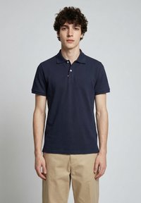 Polo bleu marine en coton texturé, avec un col classique, des manches courtes et une patte de boutonnage à trois boutons ornée d'un logo.