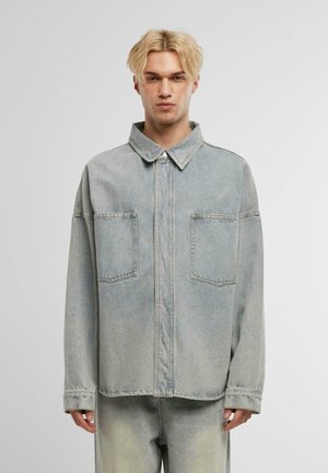 Veste en denim bleu clair avec un col à boutons, deux poches poitrine et une coupe décontractée. Comprend un léger décoloré et des détails de couture.