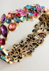Gold-tone bracelet with multicolored gemstones in various shapes, including pear, oval, and round. Intricate textured metal detailing.