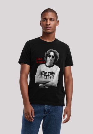 Black t-shirt featuring a gray graphic of a man in sunglasses with "john lennon" above and "NEW YORK CITY" below in bold text.