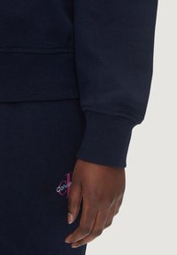 Marinblå sweatshirt med ribbad muddar och nederkant, med en rosa Calvin Klein-logotyp på bröstet, slät yta och avslappnad passform.