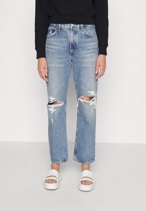 Jasnoniebieskie dżinsy z dziurami na kolanach, klasyczny krój prosty, średni stan, z postrzępionym dołem, w zestawieniu z białymi klapkami.