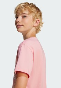 Light pink t-shirt with short sleeves, round neckline, and a smooth texture. Features printed text on the front in a contrasting color.