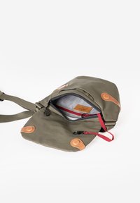 Borsa a tracolla verde oliva con patta aperta, che mostra la tasca con zip interna, la tracolla rossa e dettagli in pelle marrone sullo sfondo bianco.