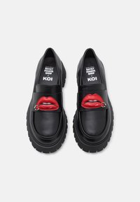 Black leather loafers with red lips design on the front, featuring a chunky sole and silver hardware accent. Textured surface detailing.