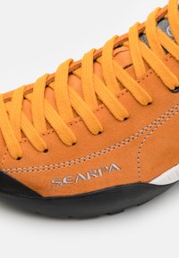 Orange mockasins klätterskor med livfulla gula snören, en svart gummisula och grå sömmar. Har varumärket "SCARPA" i silver.