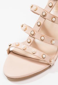 Sandale beige avec trois fines brides ornées de petites perles blanches rondes montées sur des bases dorées.