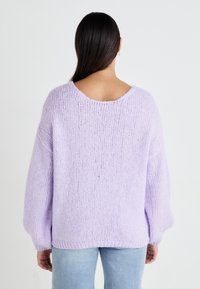 Oversized lila gebreide trui met een brede ronde halslijn en drop shoulders, met een gestructureerde, losse weving. Gecombineerd met lichtblauwe jeans.
