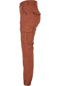 Pantalon cargo slim couleur rouille avec plusieurs poches à rabat, passants de ceinture et bas élastiqués, vu de profil.