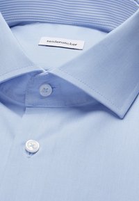 Camicia azzurra chiaro con colletto appuntito, due bottoni bianchi chiusi e etichetta "seidensticker" visibile all'interno del colletto.